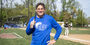Image of a person wearing a blue shirt and holding up baseball bat on a field.