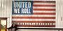 Brasten stands near an American flag that reads "United We Roll" and "Harley-Davidson."