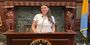 Giordano stands behind a podium in the mayor’s office