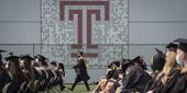 a graduate in robe and cap walks in front of large Temple T