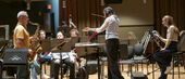 Image of Matthew Levy soloing with the wind symphony. Patricia Cornett conducts while Emma O'Halloran observes.