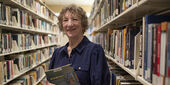 Sandi Thompson standing in the book stacks with a book in her hands at Ambler Campus Library