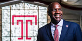 Arthur Johnson, in suit, smiling in front of Temple logo