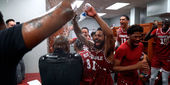 Temple basketball players wearing cherry and white jerseys, smiling brightly douse water on a coach inside the team locker room.