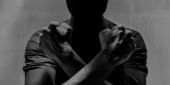 A black and white image of a man crossing his wrists over his chest in the Wakanda Forever gesture.