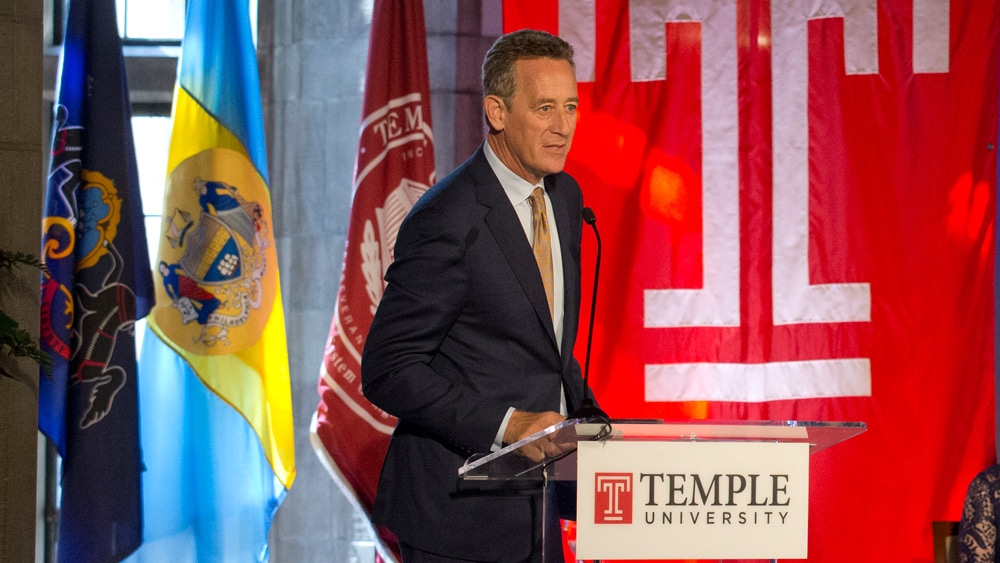 A man in a black suit standing at a podium.
