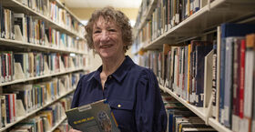Sandi Thompson standing in the book stacks with a book in her hands at Ambler Campus Library