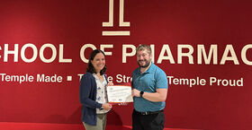Faculty co-advisors in front of a red wall with the Temple T and the award